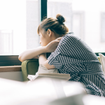 Kelly: CEFALY "me cambió la vida" a woman sitting on a couch looking out a window with a book balanced on her lap