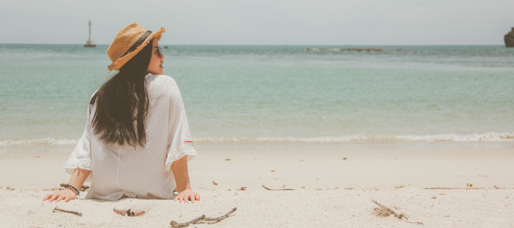 Tips on How to Avoid Migraine When Traveling and Flying woman sitting on sand in front of ocean