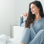 Stratégies de rentrée scolaire pour les élèves souffrant de migraine Une femme souriante en pyjama est assise sur un lit, s’étirant les bras